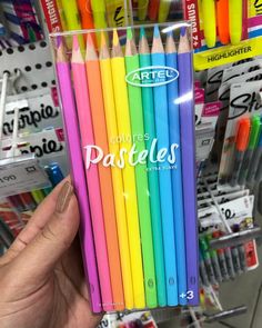 a person holding a box of colored pencils in front of a store display case