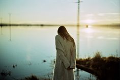 a woman standing in front of a body of water with her back to the camera