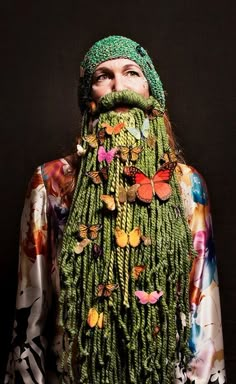 a woman with long green hair wearing a hat and scarf covered in butterflies on her face