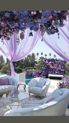 a living room filled with lots of furniture under a purple drape covered canopy over a swimming pool