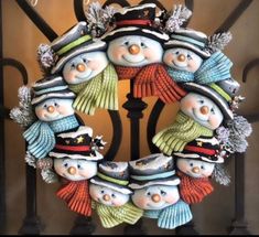 a christmas wreath with snowmen and hats hanging on a wrought iron gate that reads clay magic inc