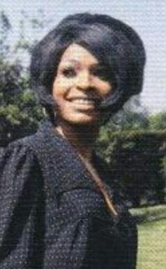 an old photo of a woman in a black dress and hat smiling for the camera