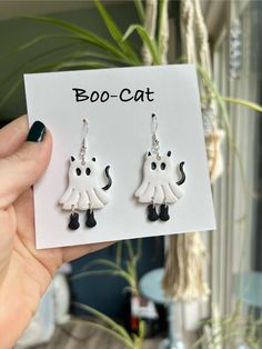 a pair of white and black cat earrings on a card next to a potted plant