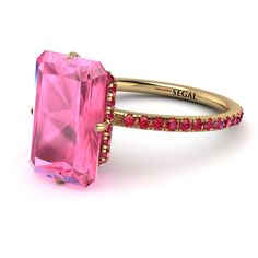 a pink tourmaline ring with red stones on the sides and gold band, set against a white background