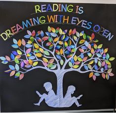 a sign that reads reading is dreaming with eyes open and two children sitting under a tree