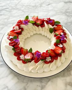 a white plate topped with a cake covered in strawberries and purple orchids on top of a marble counter