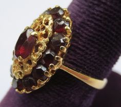 This ring looks so regal! The deep red garnets against the rich colored 18k gold compliment each other beautifully. Dating from the early 1900's-40's and hallmarked in the interior 750 and 176AAL. Has been tested to ensure the golds purity. Rings size is 6 1/2 and is ready to be worn and admired! The halo setting measures 11/16 by 7/16 of an inch. Stones are all held securely in place. Center garnet measures 6.12mm by 4.25mm. Some stones have light surface wear as to be expected with a ring of s Antique Yellow Gold Multi-stone Ruby Ring, Antique Multi-stone Ruby Ring In Yellow Gold, Victorian Ruby Ring In Yellow Gold With Intricate Design, Victorian Yellow Gold Ruby Ring With Intricate Design, Heirloom Gold Garnet Rings, Victorian Multi-stone Ruby Ring In Gold, Victorian Gold Ruby Ring With Multi-stone, Victorian Ruby Ring With Multi-stone In Gold, Victorian Ruby Cluster Ring With Gemstones