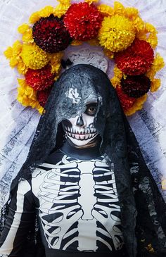 a person in a skeleton costume with flowers on the head and wreath around their neck