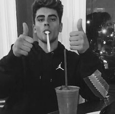 a young man is drinking from a cup with a straw in his mouth and giving the thumbs up sign