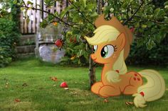 a paper cut out of a pony sitting in the grass next to an apple tree