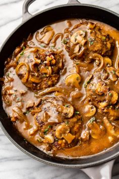 a skillet filled with meat and mushrooms covered in gravy on top of a marble counter