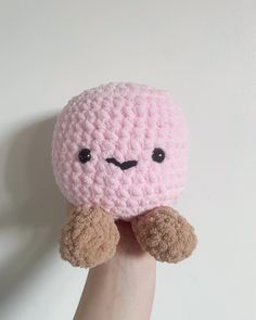 a hand holding a pink crocheted stuffed animal in it's left arm