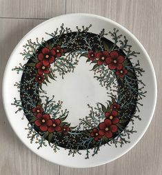 a white plate with red flowers and green leaves painted on the side, sitting on a wooden surface