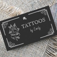 a black and white business card that says tattoos by emly on it, sitting on a piece of burlap