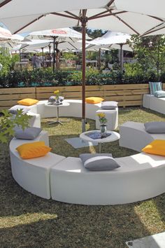 an outdoor seating area with tables and umbrellas on the grass, surrounded by plants