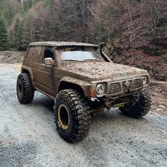 an old truck is covered in mud and parked on the side of a dirt road