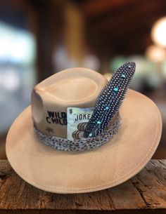 Saddle up in true Western fashion with our Sand Wild Child Felt Hat! Expertly fashioned from high-quality felt, this hat epitomizes countryside allure. Whether you're navigating the city's bustling streets or two-stepping through lively saloons, this teardrop-style hat is your steadfast companion for any occasion. Comes ready-to-wear with a leopard hat belt, Wild Child branding, lucky Joker playing card, and turquoise feather. Flat Bill Hats For Kentucky Derby, Kentucky Derby Flat Bill Hat, Felt Hats For Rodeo In Fall, Fedora Felt Hat For Kentucky Derby, Felt Hat With Flat Brim For Country Events, Fall Felt Hat For Rodeo, Winter Fedora For Country Events, Felt Material, Country Style Short Brim Felt Hat For Kentucky Derby, Winter Fedora In Felt For Country Events