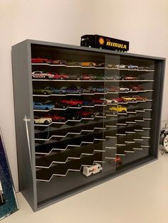 a display case filled with toy cars on top of a white table next to a clock