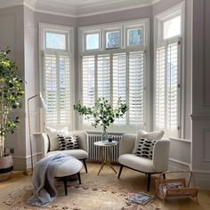 a living room filled with furniture and windows covered in white shuttered shades on top of them