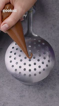 a person holding an ice cream cone in their right hand and scooping it into a colander