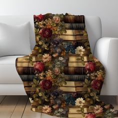 a blanket with books and flowers on it in front of a white couch next to a chair