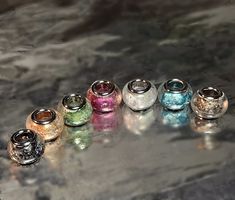 seven different colored glass jars sitting on top of a marble countertop next to each other