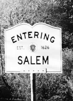 black and white photograph of a sign for salem, with trees in the back ground