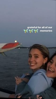 two girls are smiling while riding on a boat in the water with an airplane flying above them