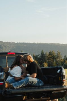 two people sitting on the back of a pickup truck with their arms around each other