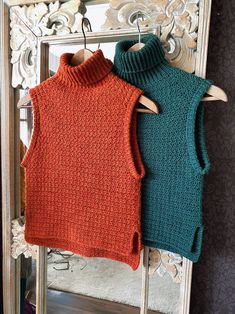 two knitted vests hanging on a clothes rack in front of a decorative mirror