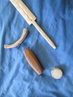 two wooden toys are laying on a blue sheet and one is holding a knife, the other has a piece of wood