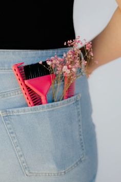 a woman is holding a pink comb and flowers in her back pocket while wearing jeans