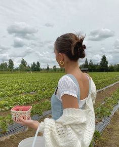 a woman holding a basket in her hand while standing next to a strawberry farm field