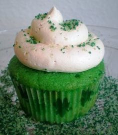 a cupcake with white frosting and green sprinkles on top is sitting in a glass bowl