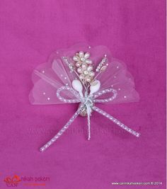 a pink and white brooch with pearls on it's wings, sitting on a purple background