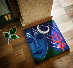 a painting is on the floor next to a plant and a doormat with a woman's face painted on it