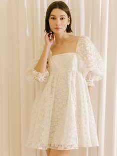 a woman in a white dress is talking on her cell phone while standing next to a curtain