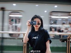 a woman taking a photo with her camera on a train platform while people are in the background