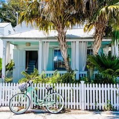 a bicycle parked in front of a white picket fence with palm trees and a house behind it