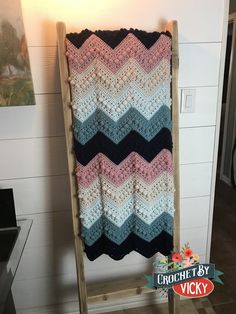 a crocheted blanket is hanging on a wooden rack next to a white wall