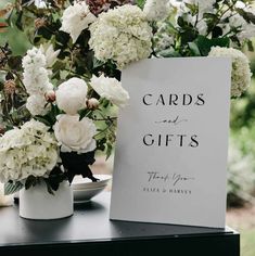 white flowers are in vases next to a card and gifts sign on a table