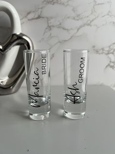 two shot glasses sitting on top of a counter next to a coffee pot and spoon