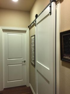 an empty hallway with two white doors and framed pictures on the wall next to it