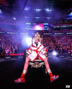 a man sitting on top of a giant chair in front of a crowd at a concert