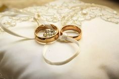 two gold wedding rings sitting on top of a white satin pillow with ribbon around it