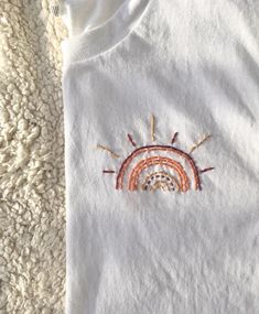 a white t - shirt with an embroidered sun and rainbow in the middle on a carpet