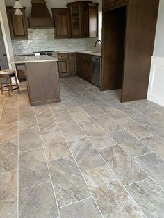 a kitchen with brown cabinets and tile flooring in the middle of an empty room