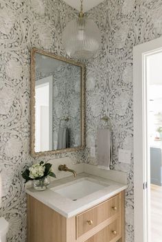 a bathroom with wallpaper and a mirror above the sink