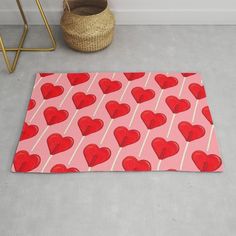 a pink rug with red hearts on it next to a wicker basket and potted plant