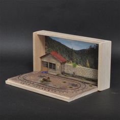 a wooden box with a miniature model of a house and train tracks in the front